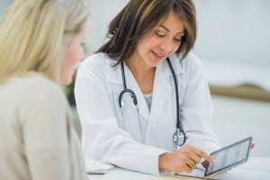 A pregnant Caucasian woman in a doctor's office with her doctor. They are discussing medical information on a tablet.